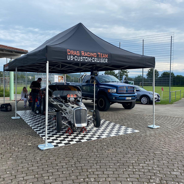 Black 8x4 gazebo with Drag Racing Team logo covers a flaming vintage car and is fixed to the ground with Ecotent gazebo weights