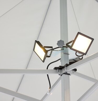 Der LED-Scheinwerfer, bestehend aus 3 Spots, ist am Mittelpfosten des Faltpavillons montiert. Der LED-Scheinwerfer ist an.