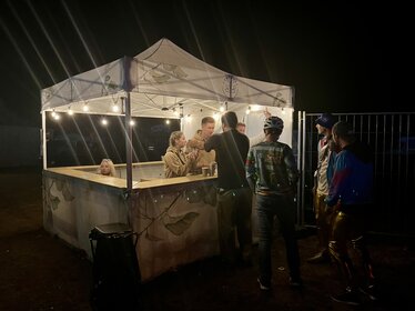 Bedruckter Ecotent® Faltpavillon mit Blätter-Design, bei Nacht als Outdoor-Bar genutzt, mit Beleuchtung und Gästen an der Theke.