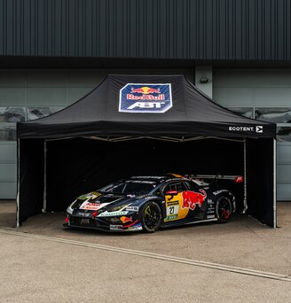 Vor einem Garagentor steht ein getuntes und bedrucktes Rennauto unter einem bedruckten Ecotent Faltpavillion Serie E1 der Größe 4,5 x 3 Meter.